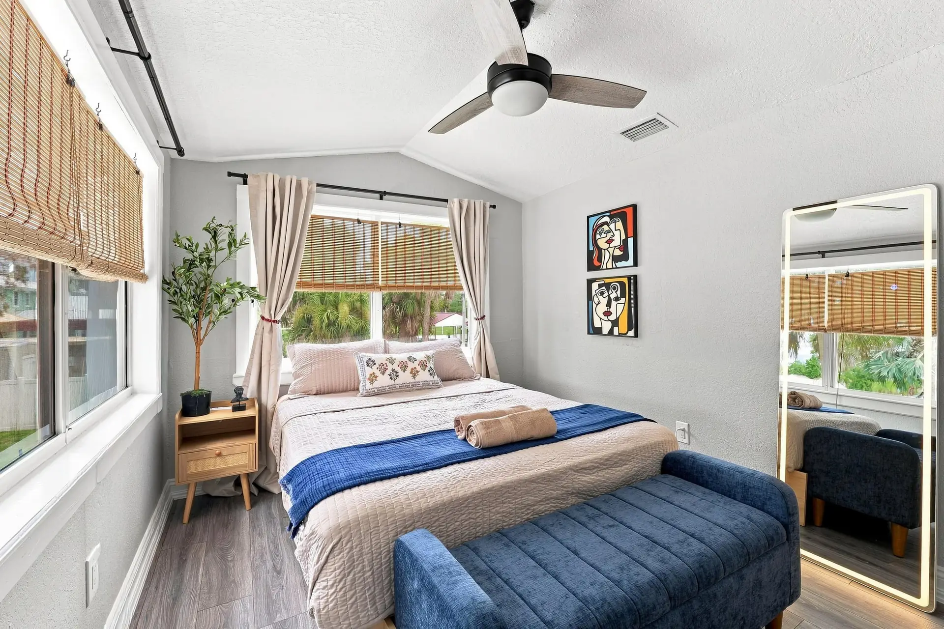 Queen bedroom with a blue velvet storage bench at the foot of the bed, a full-length lighted mirror and framed pop-art prints