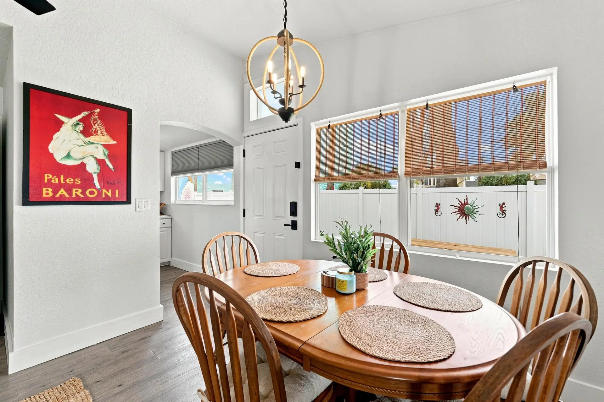 Dining table with six spindle-back wooden chairs, woven placemats and a rattan globe chandelier beside the front door
